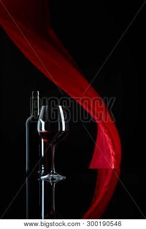 Wineglass And Bottle Of Red Wine On A Black Reflective Background.