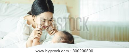 Panoramic Banner Image Of Side View Of A Young Asian Mother Hands Holding Newborn Baby Feet On A Whi