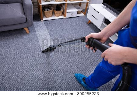 Low Section Of A Male Janitor Cleaning Carpet With Vacuum Cleaning In The Living Room