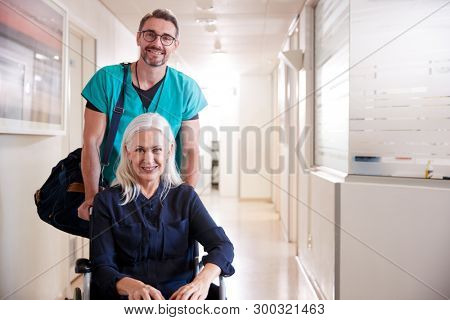 Male Orderly Pushing Senior Female Patient Being Discharged From Hospital In Wheelchair