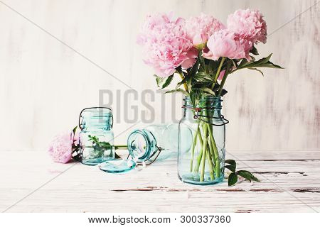 Beautiful Pink Peony Flowers In An Antique Blue Mason Jar Over A White Rustic Wood Table Background 