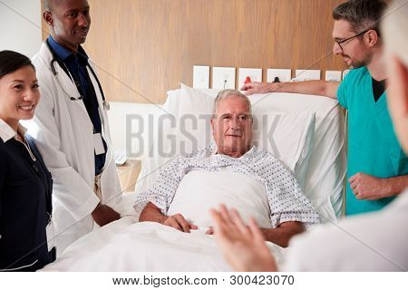 Medical Team On Rounds Meeting Around Bed Of Senior Male Patient