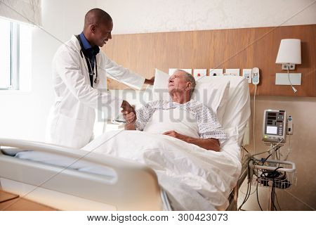 Doctor Shaking Hands With Senior Male Patient In Hospital Bed In Geriatric Unit