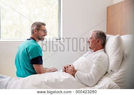 Surgeon Visiting And Talking With Senior Male Patient In Hospital Bed In Geriatric Unit