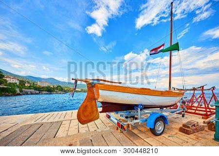 Lovran, Croatia. Sailing wooden boat at piers by sea. Boat trailer for yacht transportation. Sunny summer day and blue sky with clouds.