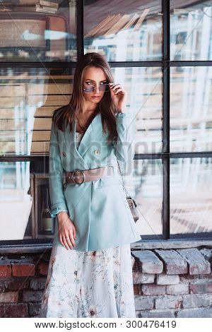Beautiful Young Blonde Girl With Long Hair In A Flower Dress, A Mint Jacket, A Wide Belt At The Wais