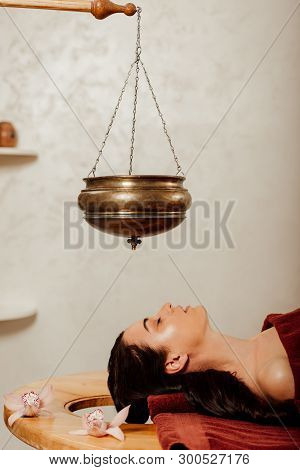 Side View Of Woman Lying Under Shirodhara Vessel During Ayurvedic Procedure
