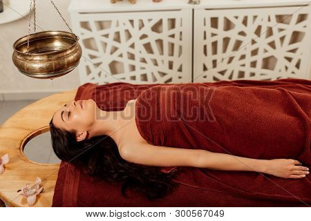 Relaxed Young Woman Lying Under Shirodhara Vessel During Ayurvedic Procedure