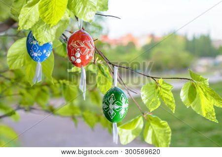 Grean Easter Background With Painted Wooden Eggs Hanging From Tree Branches. This Image Is Blurred, 