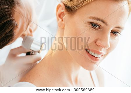 Selective Focus Of Attractive Woman Smiling While Dermatologist Examining Neck With Dermatoscope
