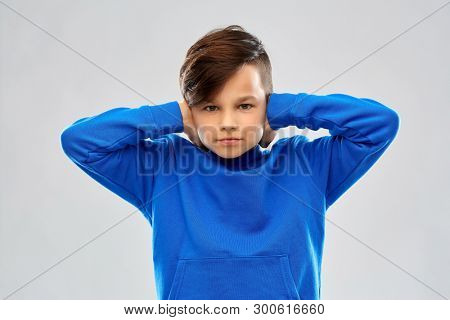 noise, stress and people concept - stressed boy in blue sweater closing ears by hands over grey background