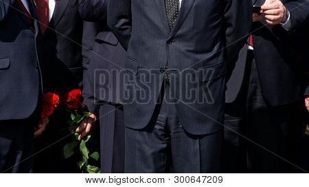 Men In Strict Black Suits With Red Flowers. Company Management. The Official Delegation. Without A F