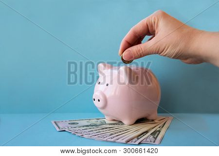 Girl Is Putting Money Into Piggy Bank With Copy Space. Concept Of Money Saving And Budgeting.