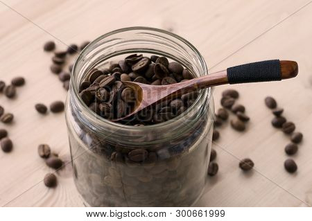 Roasted Coffee Beans In A Glass Jar With Wooden Spoon
