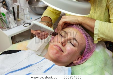A Young Girl Is Lying On Couch With A Pink Hat On Her Hair While Performing An Ultrasonic Face Clean