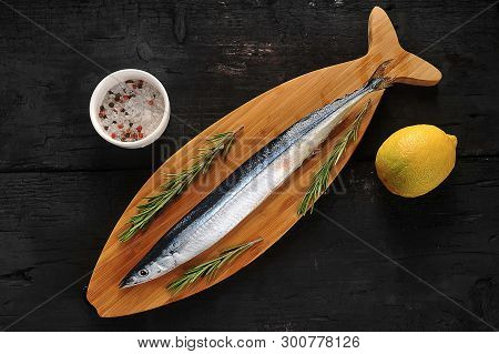 Raw Saury On A Wooden Board In The Form Of Fish With Rosemary And Lemon-top View