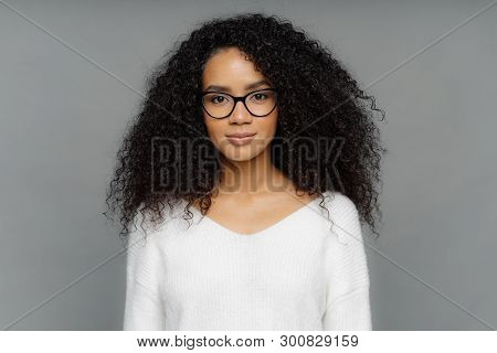 Portrait Of Serious Woman With Dark Skin, Afro Bushy Hair, Wears Big Transparent Glasses And White S