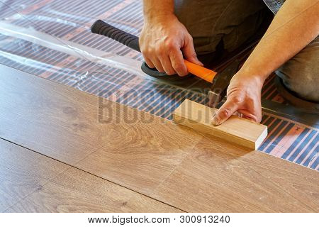 Laminate flooring. Male repairman is laying panel of  laminate floor  on a heat-insulated floor. Electrical floor heating system, radiant heating, infrared carbon heating film for floor