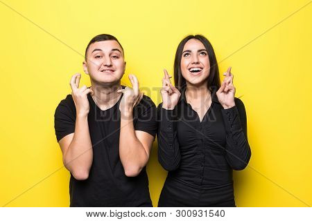 Cheerful Young Couple Cross Fingers With Hope For Good Luck On Yellow Stusio Background