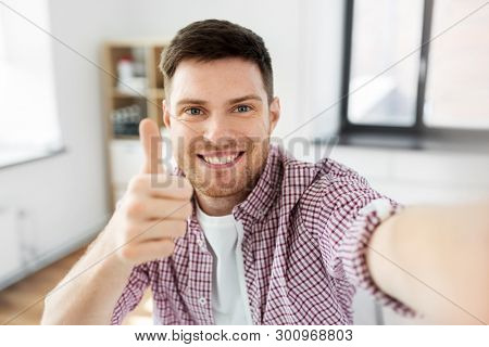 blogging, videoblog and people concept - man or blogger videoblogging or taking selfie and showing thumbs up at home
