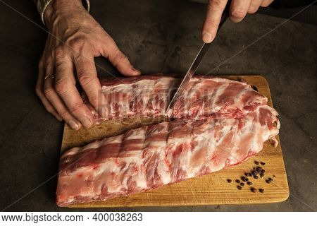 Mens Hands Cut Fresh Pork Ribs. Cooking For Frying With Garlic, On A Wooden Board, Gray Background.
