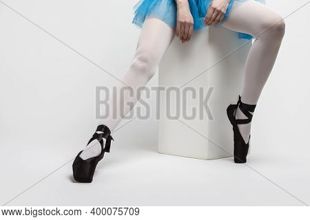 Closeup Of Legs Of Professional Female Ballet Dancer In Pointes Shoes Sitting On White Cube Against