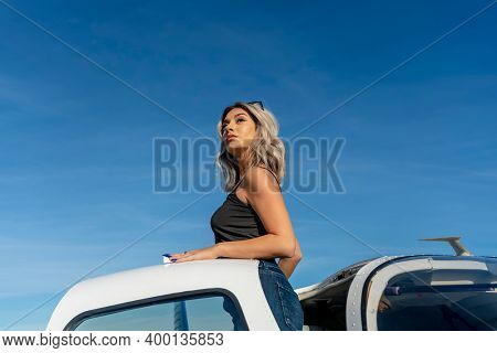 A gorgeous young blonde model poses outdoors with a single engine aircraft at a local airport