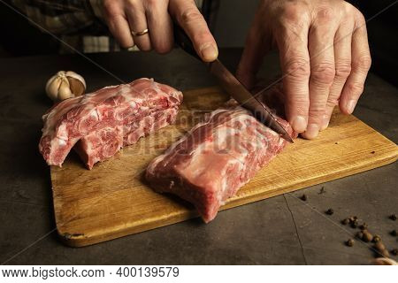 Mens Hands Cut Fresh Pork Ribs. Cooking For Frying With Garlic, On A Wooden Board, Gray Background.