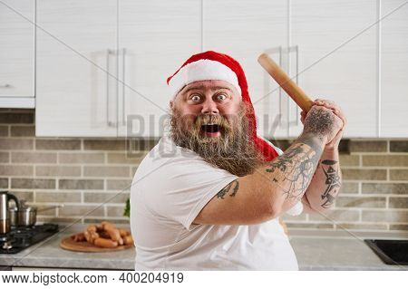 An Overweigh Man In Santa Claus Hat With Tattooed Arms Holding A Wooden Rolling Pin On Hands Like A 
