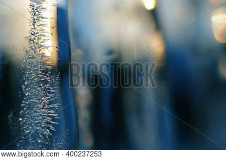 Blue And Yellow Background Of Icicles Close Up. Tinted Ice Backdrop With Winter Sunset. Frozen Water