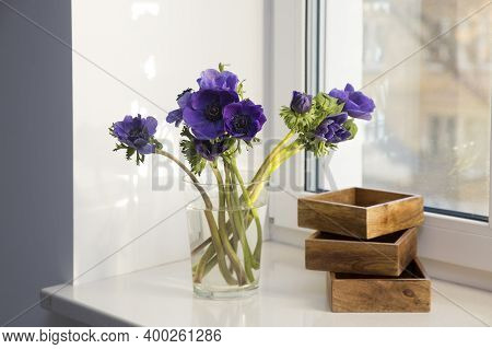 A Bouquet Of Blue Anemones In A Glass Vase Next To Three Wooden Boxes For Storing Small Items On The