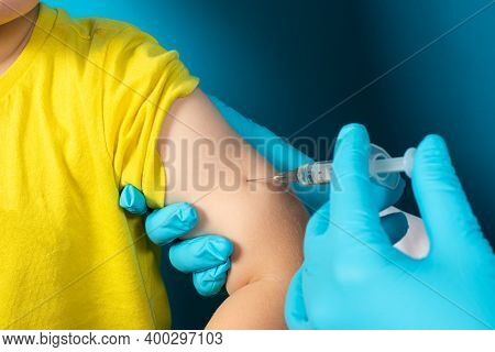 The Doctor Or Nurse Injects A Syringe To A Small Child Intramuscularly On A Blue Background. Tubercu
