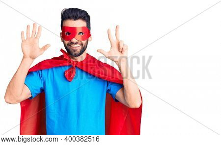 Young handsome man with beard wearing super hero costume showing and pointing up with fingers number eight while smiling confident and happy. 