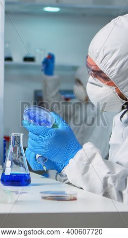 Chemist In Ppe Suit Using Micropipette For Filling Test Tubes In Modern Equipped Laboratory. Team Of