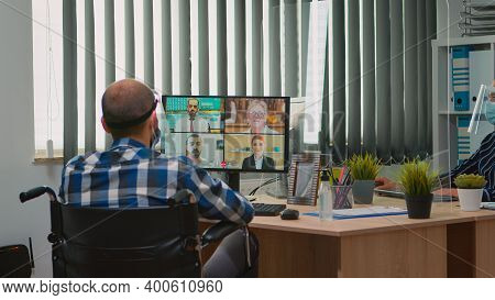 Paralysed Manager In Wheelchair Talking With Mask And Visor During Videocall Having Online Conferenc