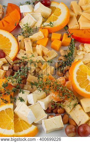 There Are Many Types Of Cheeses On The White Plate With Chopped Oranges, Grapes And Herbs. Healthy F