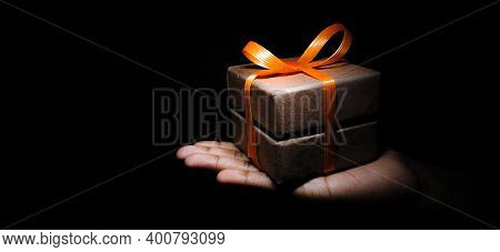 A Small Gift Box Wrapped With Rippon Placed On A Human Hand Isolated On A Black Background
