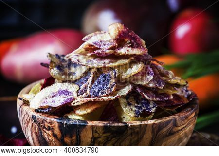 Chips From Purple And Red Potatoes In Wooden Bowl On Background Of Vegetables, Selective Focus