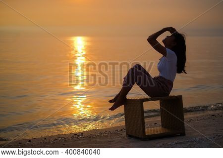 Sea Woman Sitting On Wooden Table On Sand Beach With Sea With Overlight Sunset In Summer Holidays.