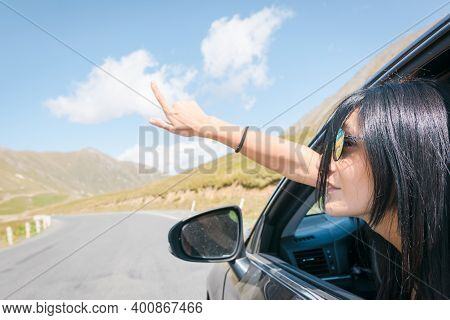 Female Caucasian Woman From Car Window Points Finger Up To Left With Asphalt Road Background. Copypa