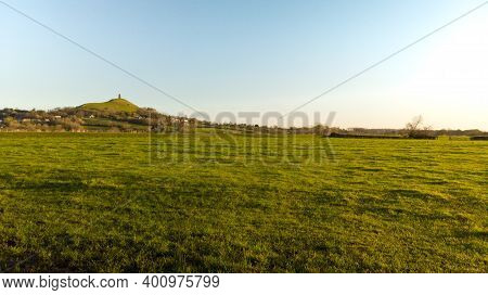 Early Morning View Of Glastonbury Tor In A Somerset Field At Golden Hour.