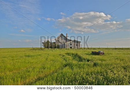 a deserted farm house is surrounded by prairie grass