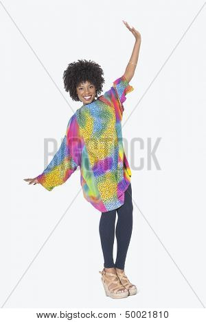 Full length portrait of happy African American woman in dashiki dancing over gray background