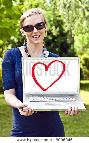 Joven rubia con la computadora en el jardín.