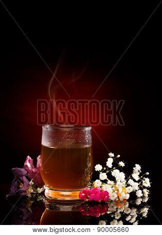 Cup of hot tea. Tea Steam. Flowers near. Red Spotlight on black background