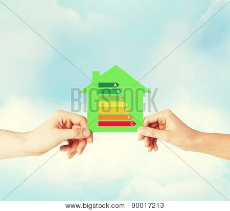 energy saving, real estate and family home concept - closeup of couple hands holding green paper house with energy efficiency rating