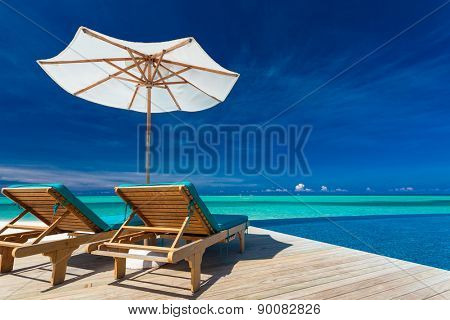 Deck chairs with umbrella overlooking infinity pool and tropical lagoon