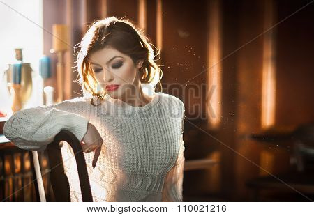 Young sensual woman sitting with window in background. Beautiful girl with white comfortable blouse