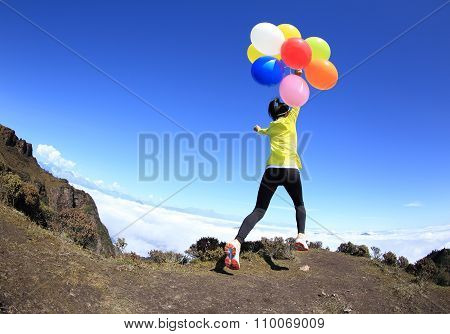 young woman on mountain peak with colorful balloons