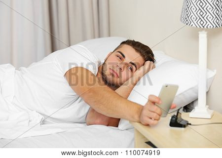 Beautiful young man waking up with mobile alarm clock
